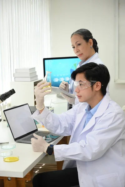 코트를 고글을 비커를 연구실에서 화학적 실험을 아시아의 재능있는 과학자가 타블렛에 — 스톡 사진