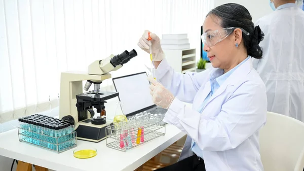 研究室で働くアジア系の高齢女性科学者や化学者は 試験管内の新しい液体試験片を調整します — ストック写真