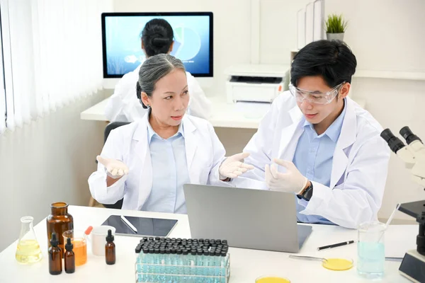 A professional asian-aged female scientist working, explaining and giving a chemical advice to her young male scientist in the lab.