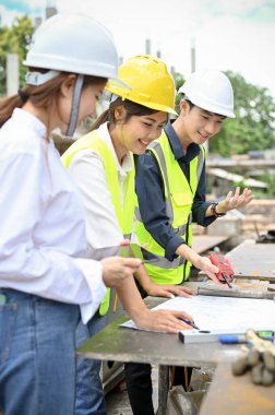 Neşeli ve profesyonel Asyalı inşaat mühendisinden oluşan bir ekip inşaat alanındaki planı birlikte inceliyor..