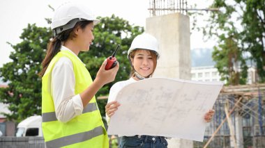 İki yetenekli genç Asyalı inşaat mühendisi ya da mimar planlara bakıyor ve şantiyede birlikte çalışıyorlar..