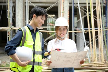 Şantiyede profesyonel erkek mühendis ile konuşurken projeye bakan çekici genç Asyalı kadın mimar..