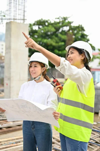 A professional Asian young female construction inspector explaining the construction plan to a female architect.