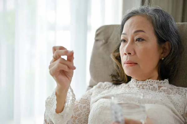ストレスの多いアジア系の中年女性は 自宅のリビングルームで薬や錠剤を服用します 健康問題の概念 — ストック写真