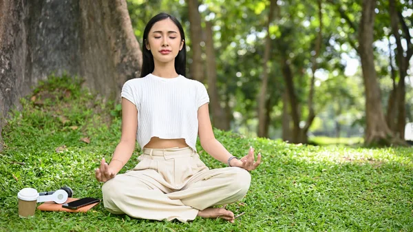 緑の公園の木の下で瞑想し 蓮のポーズに座ってカジュアルな快適な服で穏やかな若いアジアの女性 幸福と健康的なライフスタイルの概念 — ストック写真