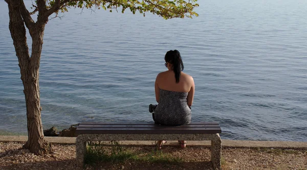 Ragazza dalla parte posteriore seduta sul sedile in legno e guardando al mare — Foto Stock