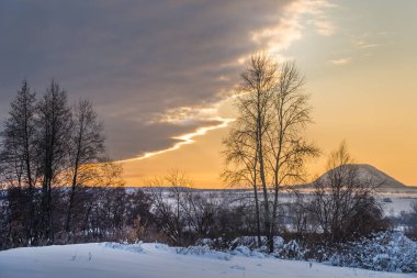 Günbatımı gökyüzünün arka planına karşı tek bir dağ. Ön planda ağaçlar.