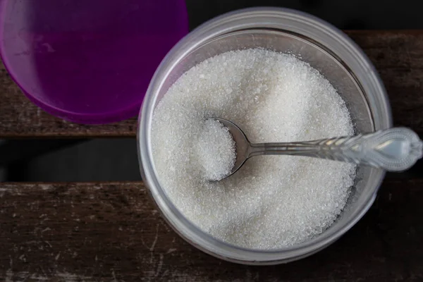 Granulated white cane sugar in a jar with a spoon.