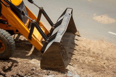 Road repair work done using heavy machinery in urban road. Bulldozer picking up excavated soil.