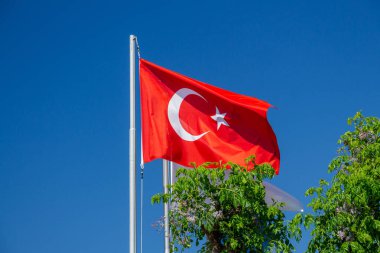 Türkiye bayrağı. Bayrak direğinde mavi gökyüzüne karşı Türk bayrağı. Beyaz yıldız ve hilal ile kırmızı bayrak. Sıklıkla 