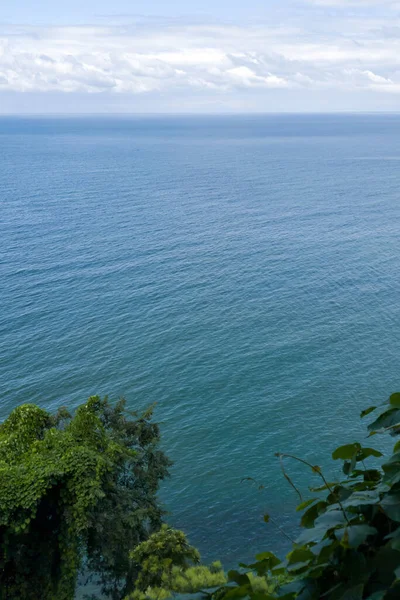 Mavi deniz yüzeyinde alçak süzülen gri bulutlarla kaplı yeşil bir dağın nefes kesici üst görüntüsü. Hafif esinti, uzayı kopyala. Uzun zamandır beklenen tatil, dinlenme ve seyahat konsepti 