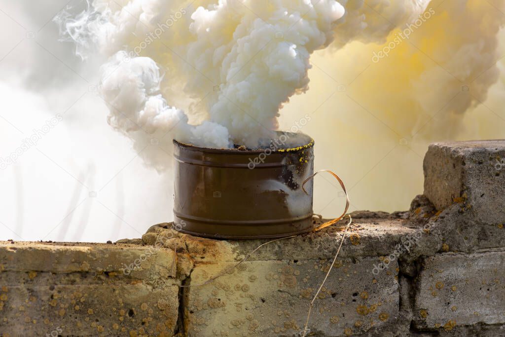 The fuming smoke grenade on a destroyed brick wall during tactical training. Used as a signaling device, target or landing zone marking device, or as a screening device for military unit movements