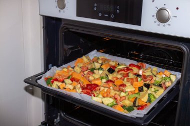 Fırında kağıt ile kaplanmış bir kabın üzerinde ince doğranmış ve baharatlı sebzeler. Patates, dolmalık biber, kabak, balkabağı ve brokoli. Vejetaryen yemekleri yakın plan.