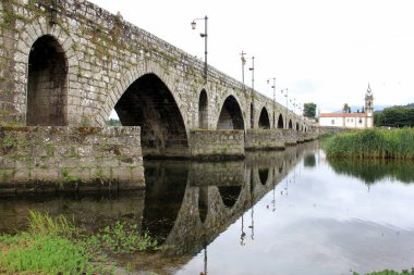 Lima Nehri üzerinde ortaçağ taş köprüsü, 18. yüzyıl Santo Antonio da Torre Velha Kilisesi nehrin karşı tarafında, Ponte de Lima, Portekiz - 20 Temmuz 2021
