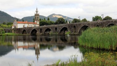 Lima Nehri üzerinde ortaçağ taş köprüsü, 18. yüzyıl Santo Antonio da Torre Velha Kilisesi nehrin karşı tarafında, Ponte de Lima, Portekiz - 20 Temmuz 2021