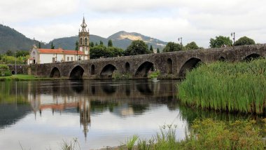 Medieval stone bridge over the Lima River, 18th-century Church of Santo Antonio da Torre Velha in the background on the opposite side of the river, Ponte de Lima, Portugal - July 20, 2021 clipart