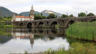 Lima Nehri üzerinde ortaçağ taş köprüsü, 18. yüzyıl Santo Antonio da Torre Velha Kilisesi nehrin karşı tarafında, Ponte de Lima, Portekiz - 20 Temmuz 2021