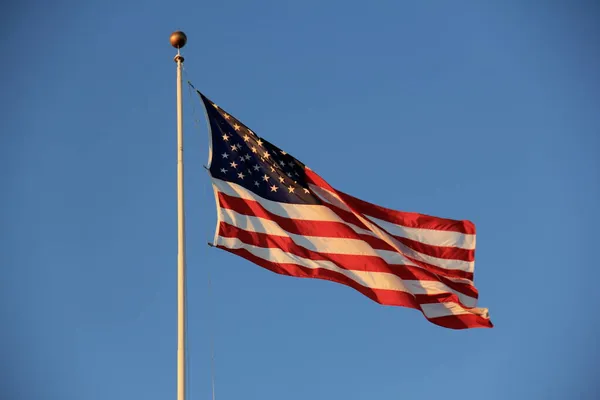日没の光の中で青い空の背景にスタッフに飛ぶ米国の旗 — ストック写真