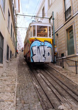 Slopped cobblestone street with cable car on rail tracks in the old town, in afternoon shadows, Lisbon, Portugal - July 23, 2021