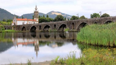 Lima Nehri üzerinde ortaçağ taş köprüsü, 18. yüzyıl Santo Antonio da Torre Velha Kilisesi nehrin karşı tarafında, Ponte de Lima, Portekiz - 20 Temmuz 2021