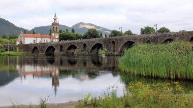 Lima Nehri üzerinde ortaçağ taş köprüsü, 18. yüzyıl Santo Antonio da Torre Velha Kilisesi nehrin karşı tarafında, Ponte de Lima, Portekiz - 20 Temmuz 2021