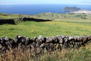 Kırsal alan, yeşil çayırlar ve taş çitler, okyanus kıyısına doğru eğimli, Serra da Ribeirinha 'nın manzarası, arka planda Brezilya Dağı ve Angra do Heroismo, Terceira Adası, Azores, Portekiz - 29 Temmuz 2022