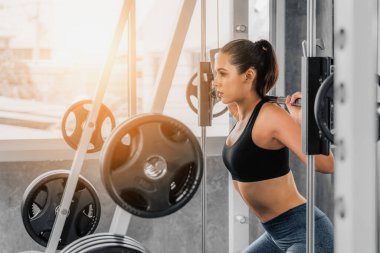 Spor kıyafetleriyle spor yapan beyaz atletik kadın spor salonunda vücut geliştirmek için halter kaldırıyor ve ışık saçan bir yaşam tarzı için spor salonunda spor yapıyor.