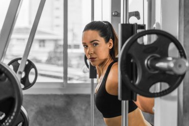 Spor kıyafetleriyle spor yapan beyaz atletik kadın spor salonunda vücut geliştirmek için halter kaldırıyor ve yaşam tarzını iyileştirmek için spor salonunda spor yapıyor.