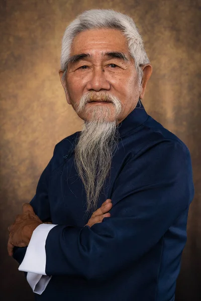 studio portrait of old man with white hair and beard in tradional chinese clothing on studio backdrop background