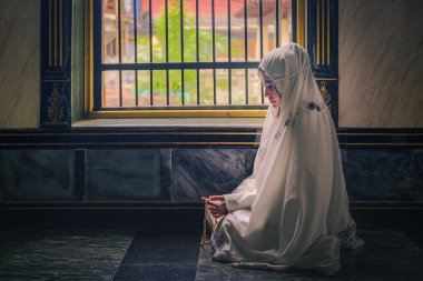 Jihab 'daki Asyalı genç kadın camide oturmuş Allah' ın lütfu için dua ediyor.