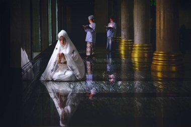 Müslüman kadınlar tesettürde ve Müslüman erkekler camide birlikte namaz kılar ve Kuran okurlar.