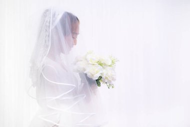 Beyaz önlüklü Asyalı gelinin beyaz arka planda çiçek buketi tutan stüdyo portresi.