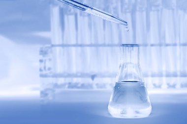science and laboratory background of lab flask with dropper drop some blue liquid with blurred background of test tubesin laboratory, laboratory research and development concept