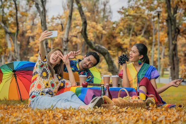 LGBTQ people friends enjoying picnic together in park in autumn and having selfie. Concept of LGBTQ people lifestyle