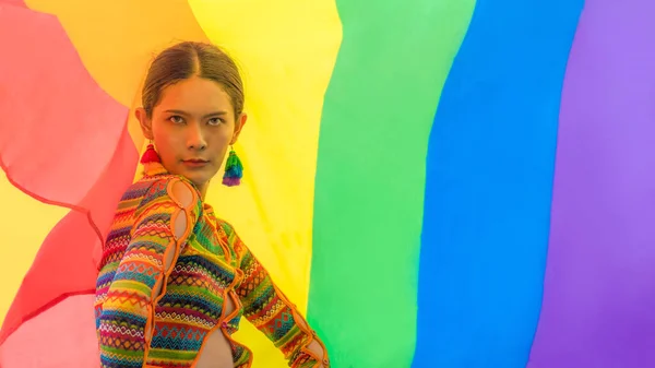 portrait of asian transgender person in colorful dress posing with rainbow pride flag to celebrate of LGBTQIA right in equality and diversity in pride month