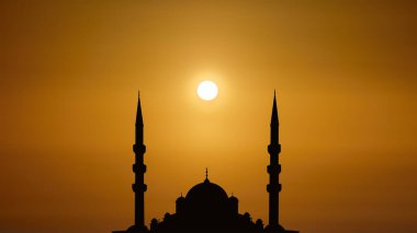 Kubbeli siluet İslami cami manzarası ve gündoğumunun arka planında iki kule.