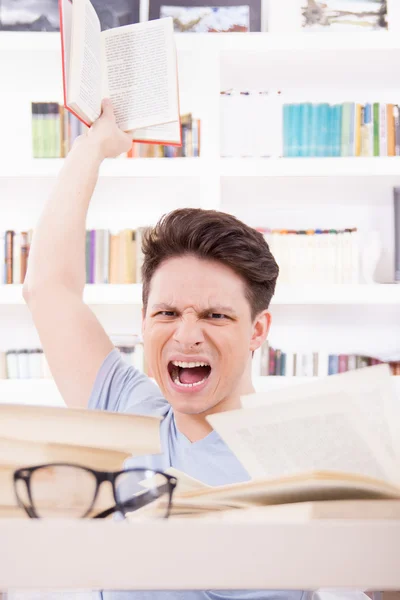 Angry student with expression surrounded by books throwing a bo — Stock Photo, Image