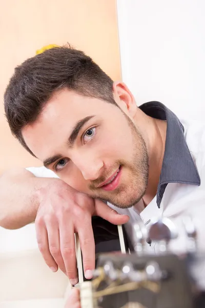 Handsome man leaning on his guitar and smiling — Stock Photo, Image