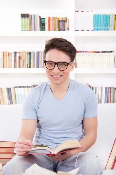Usmívající se muž s brýlemi, čtení knihy na gauči — Stock fotografie