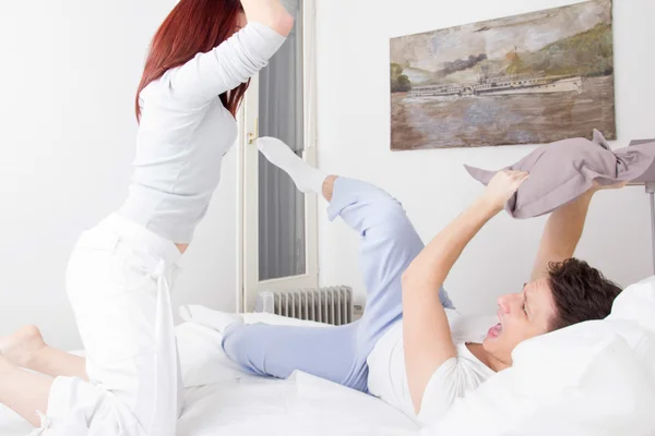 Rozzlobený pár bojuje s polštáři v posteli s confli — Stock fotografie