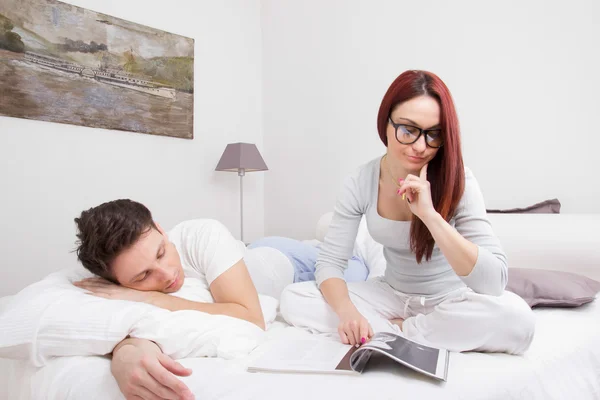 Frau liest Buch im Bett und Mann schläft neben ihr — Stockfoto