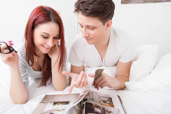 Jovem casal feliz leitura revista juntos na cama — Fotografia de Stock