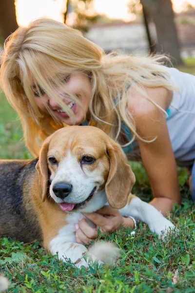 Smiling blonde woman in jeans lying and playing with dog on the — Stock Photo, Image