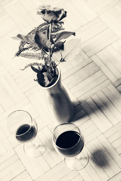 Dos copas de vino y una rosa roja con hojas en un jarrón — Foto de Stock