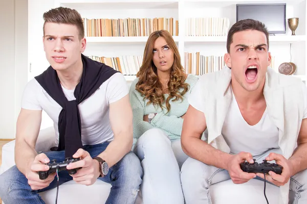 Скучающие женщины между двумя страстными мужчинами, играющими в видеоигры — стоковое фото