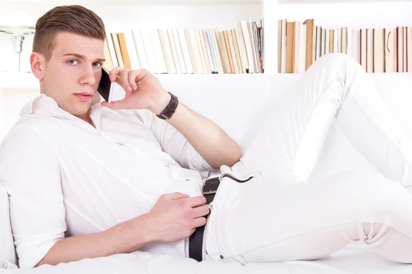 Соблазнительный молодой человек лежит на диване и разговаривает по телефону — стоковое фото