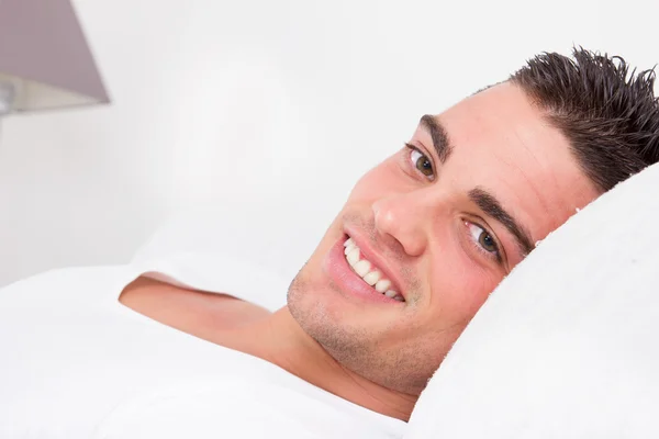 Bonito sensual homem sorrindo deitado no cama — Fotografia de Stock