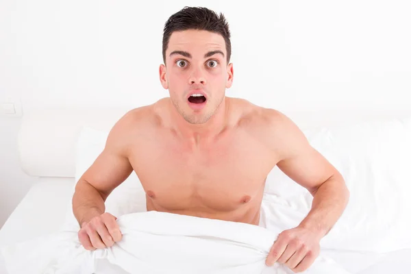 Chockad halv naken ung man i sängen, tittar ner på hans underwe Stockbild