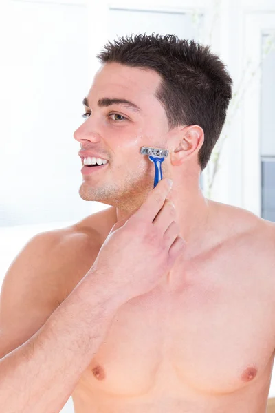 Привабливий чоловік голиться обличчям тримає бритву — стокове фото