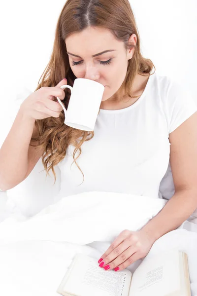 Genç kadın zevk okuma ve yatakta kahve içme — Stok fotoğraf